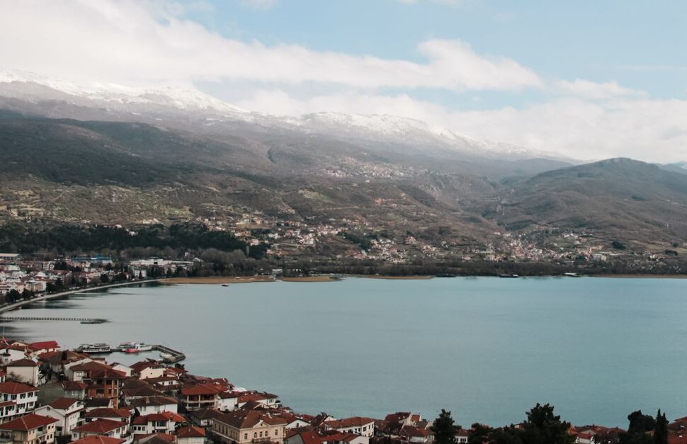 Town with red-roofed houses along a calm blue lake, mountains with snow on the peaks in the background